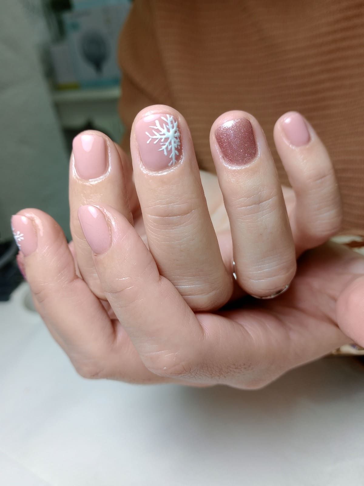 Primer plano de unas manos cuidadas con uñas decoradas con purpurina rosa y copos de nieve sobre una superficie blanca