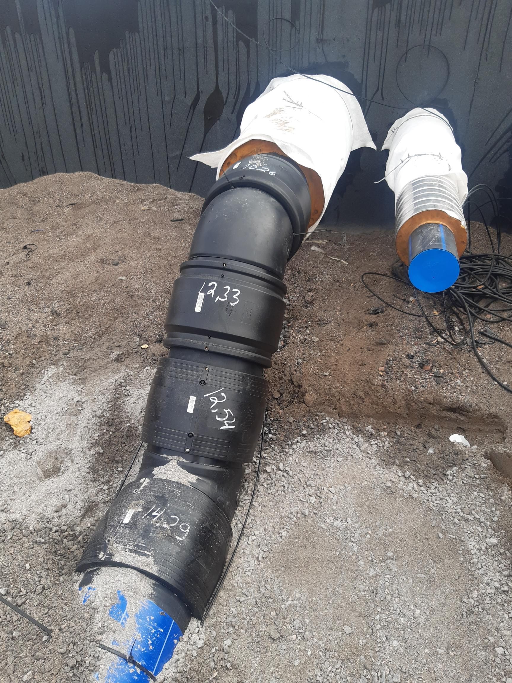 Musta putki sinisillä päillä yhdistyy valkoiseen kanavaan karkeaa seinää ja soramaata vasten