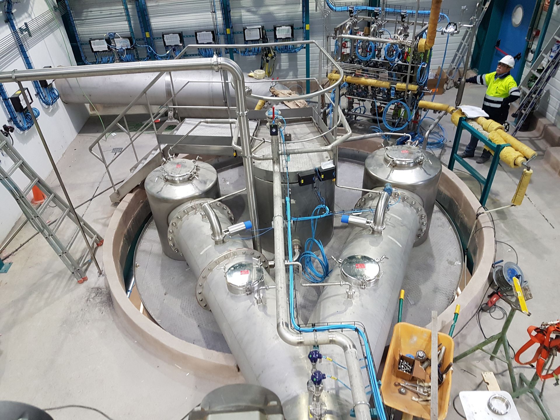 Installation industrielle avec réservoirs et tuyaux en acier inoxydable ; un ouvrier observe de côté.