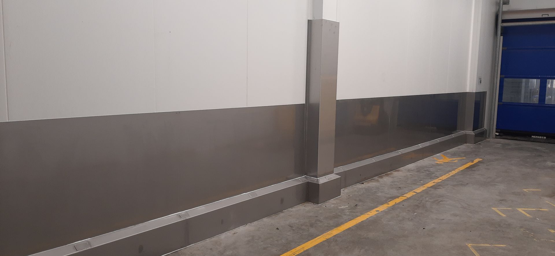 Intérieur d'entrepôt avec murs gris et blancs, ligne jaune et porte bleue.