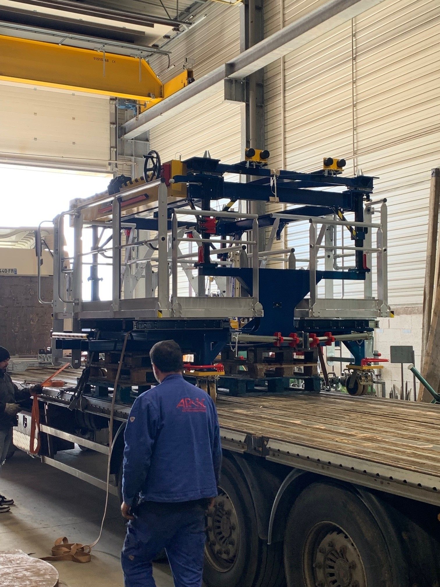 Des hommes déchargent de gros équipements industriels d'un camion, à l'intérieur d'un entrepôt.