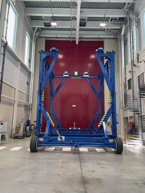 Cadre en métal bleu sur roulettes dans une pièce blanche, porte rouge en arrière-plan.