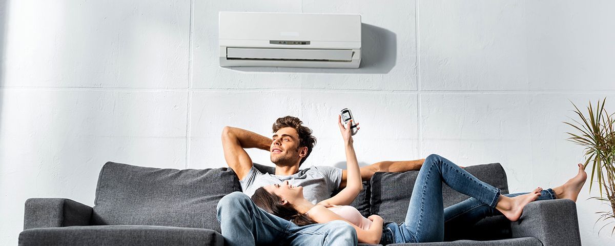 Photographie d'un couple installé sur le canapé profitant de l'air frais du climatiseur