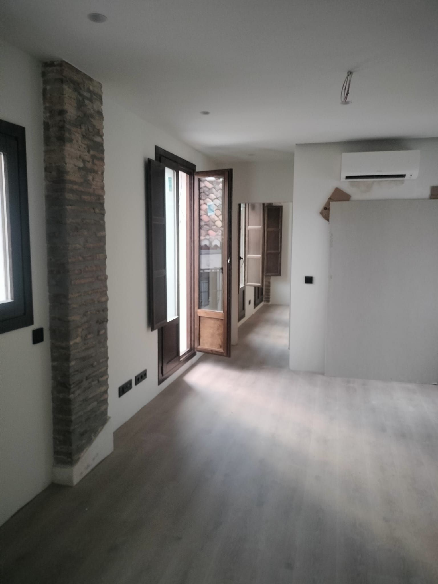 Interior de apartamento moderno vacío con suelos de madera clara, paredes blancas y puertas de balcón abiertas.