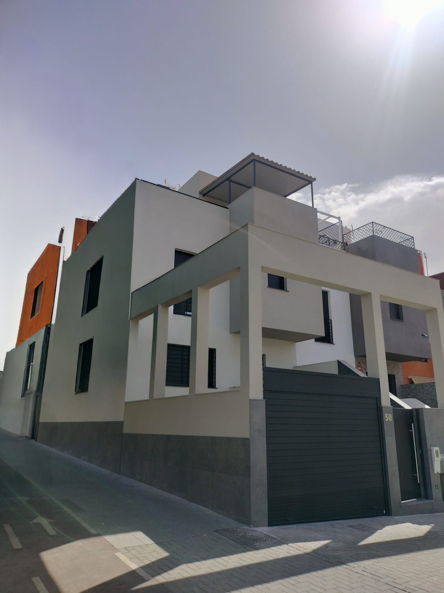 Moderna casa blanca de dos plantas con detalles naranjas y una puerta negra bajo un cielo brillante.