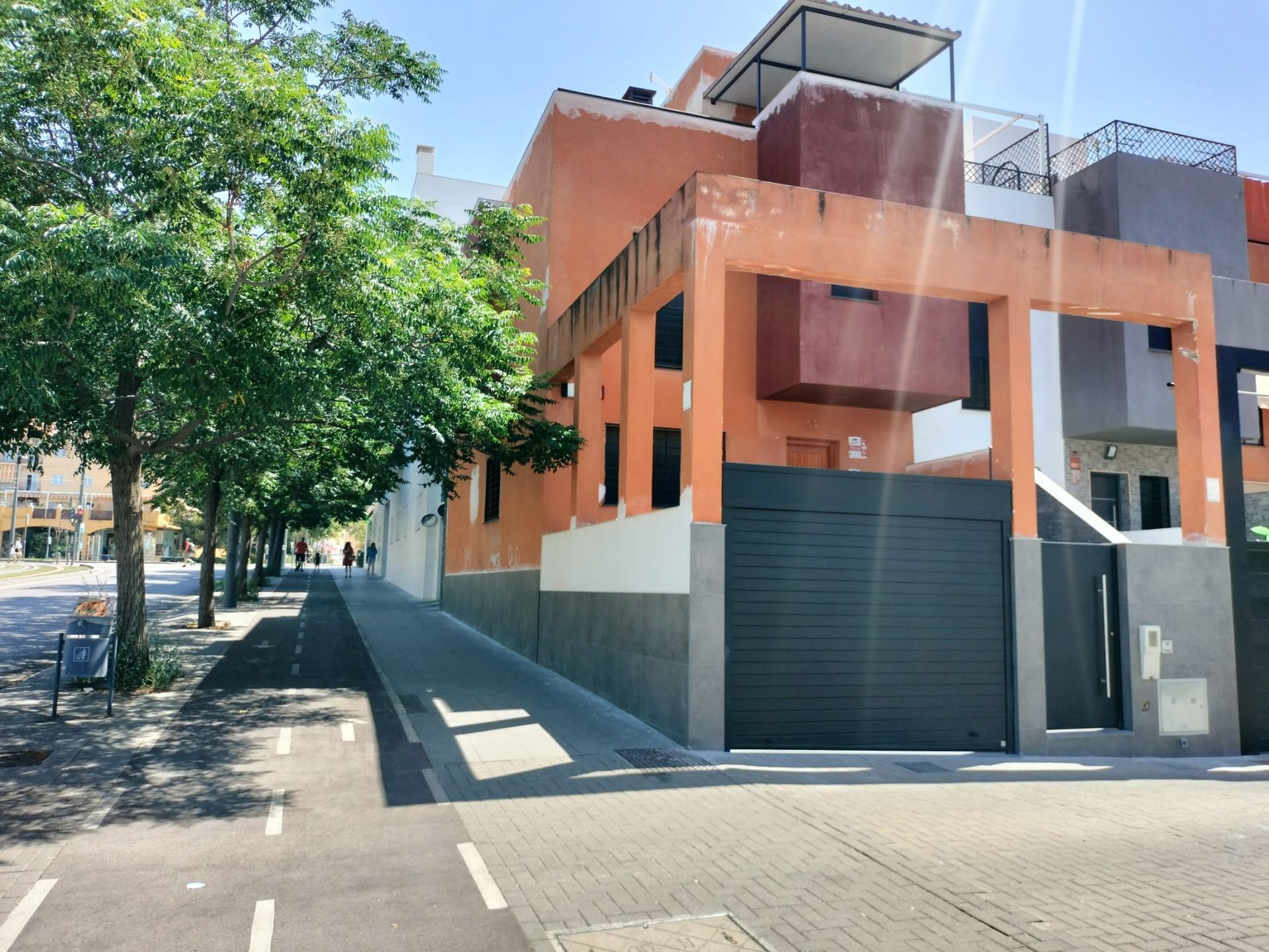 Edificio moderno de color naranja en una calle tranquila, junto a árboles y una acera estrecha.