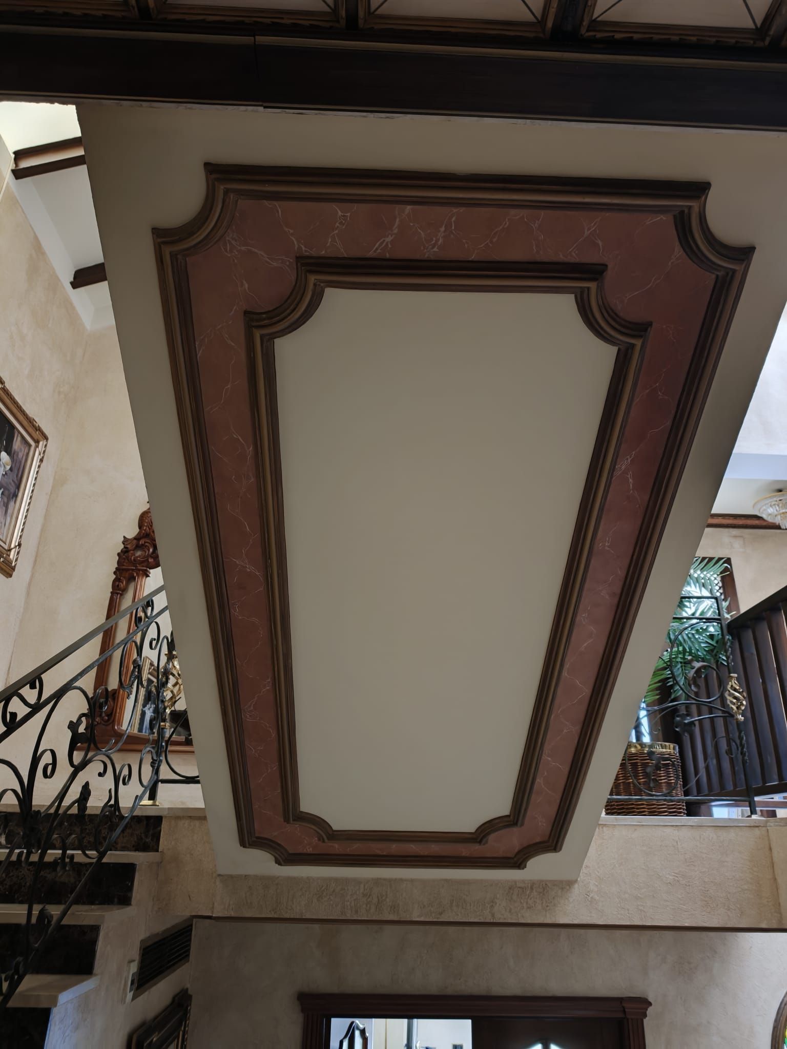 Panel decorativo de techo artesonado con moldura marrón y centro color crema en una escalera interior.