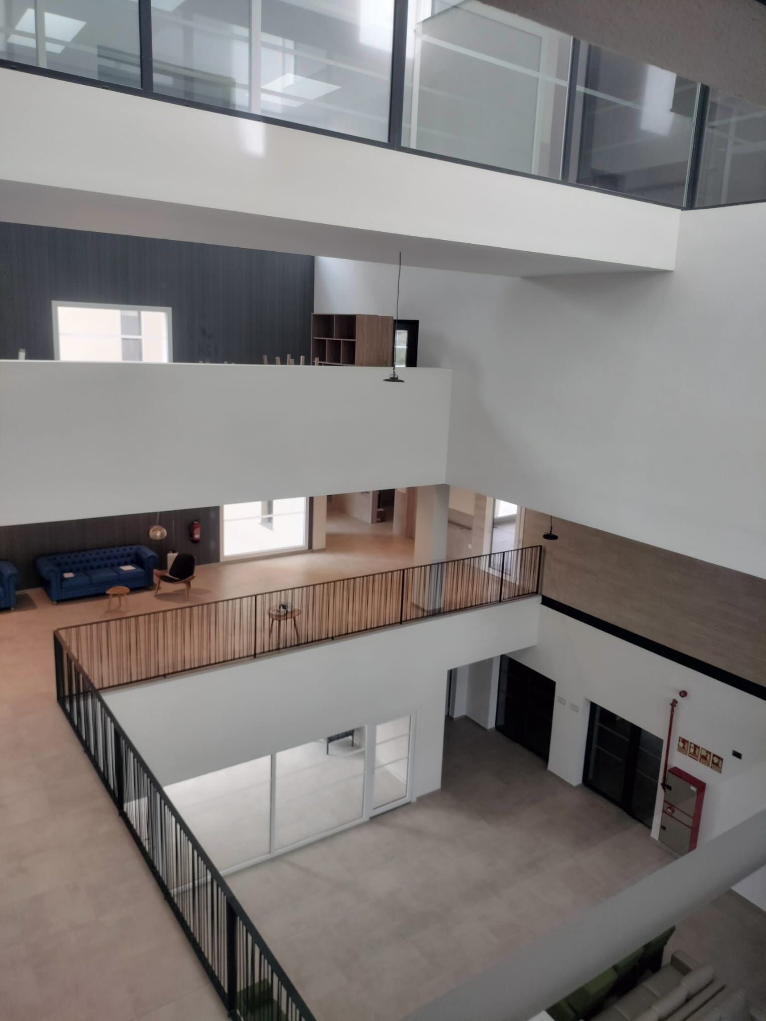 Interior moderno con atrio, balcones, barandillas de cristal y una zona de estar en una planta superior.