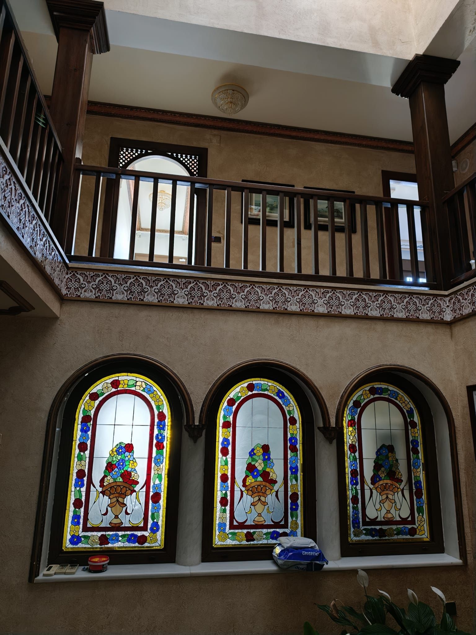 Balcón interior con vidrieras arqueadas y barandilla de madera en un luminoso pasillo.