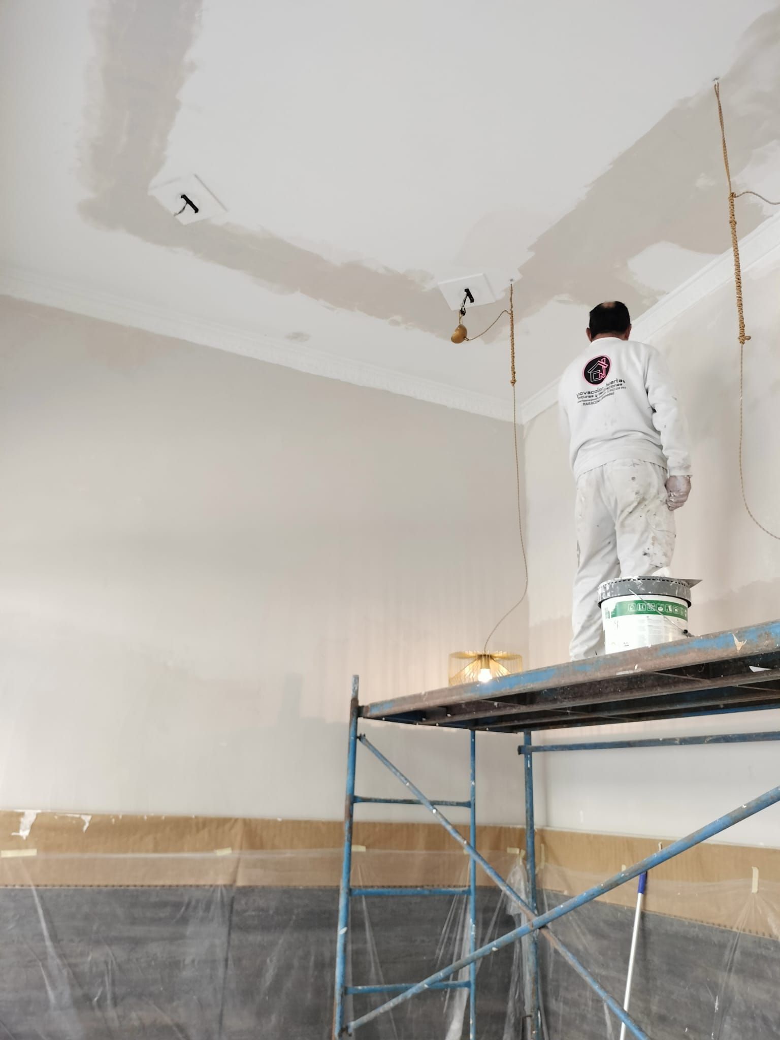 Persona pintando el techo desde un andamio en una habitación en reforma.