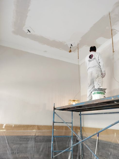 Persona pintando el techo desde un andamio en una habitación en reforma.