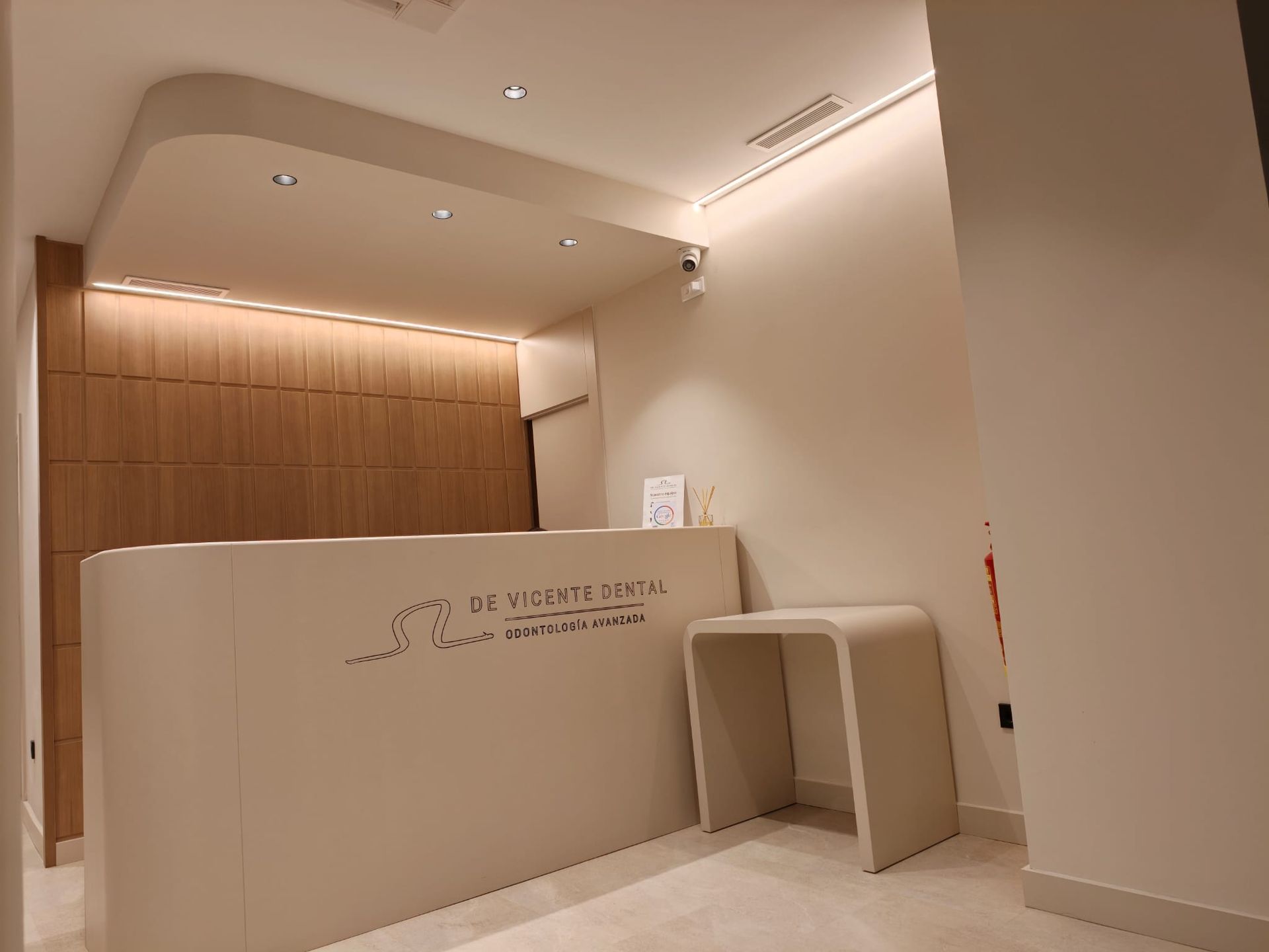 Área de recepción moderna y minimalista con escritorio blanco, pared de madera y luces empotradas en el techo.