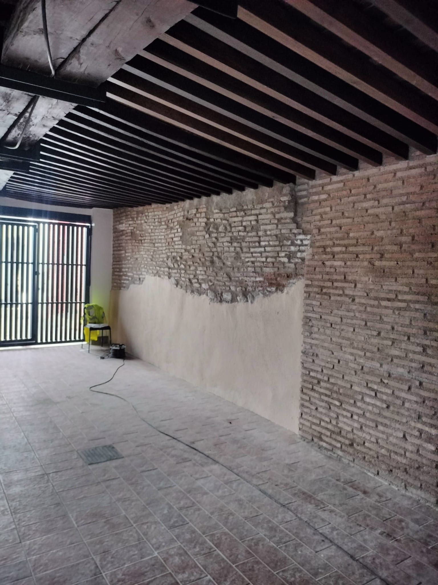 Pasarela cubierta con pared de ladrillo visto, techo de listones y una puerta al final.