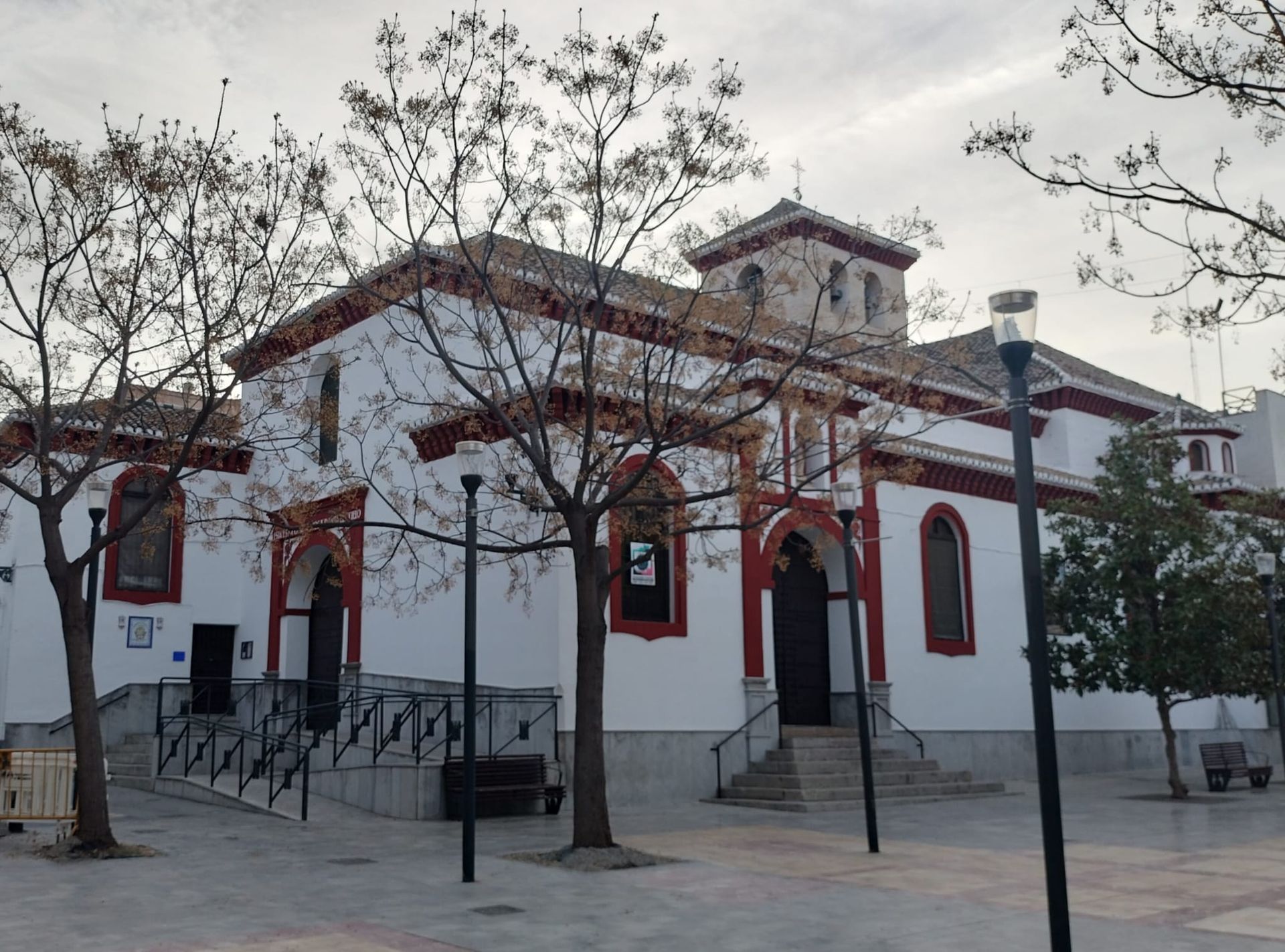 Edificio blanco con detalles rojos y ventanas arqueadas en una tranquila plaza al atardecer.