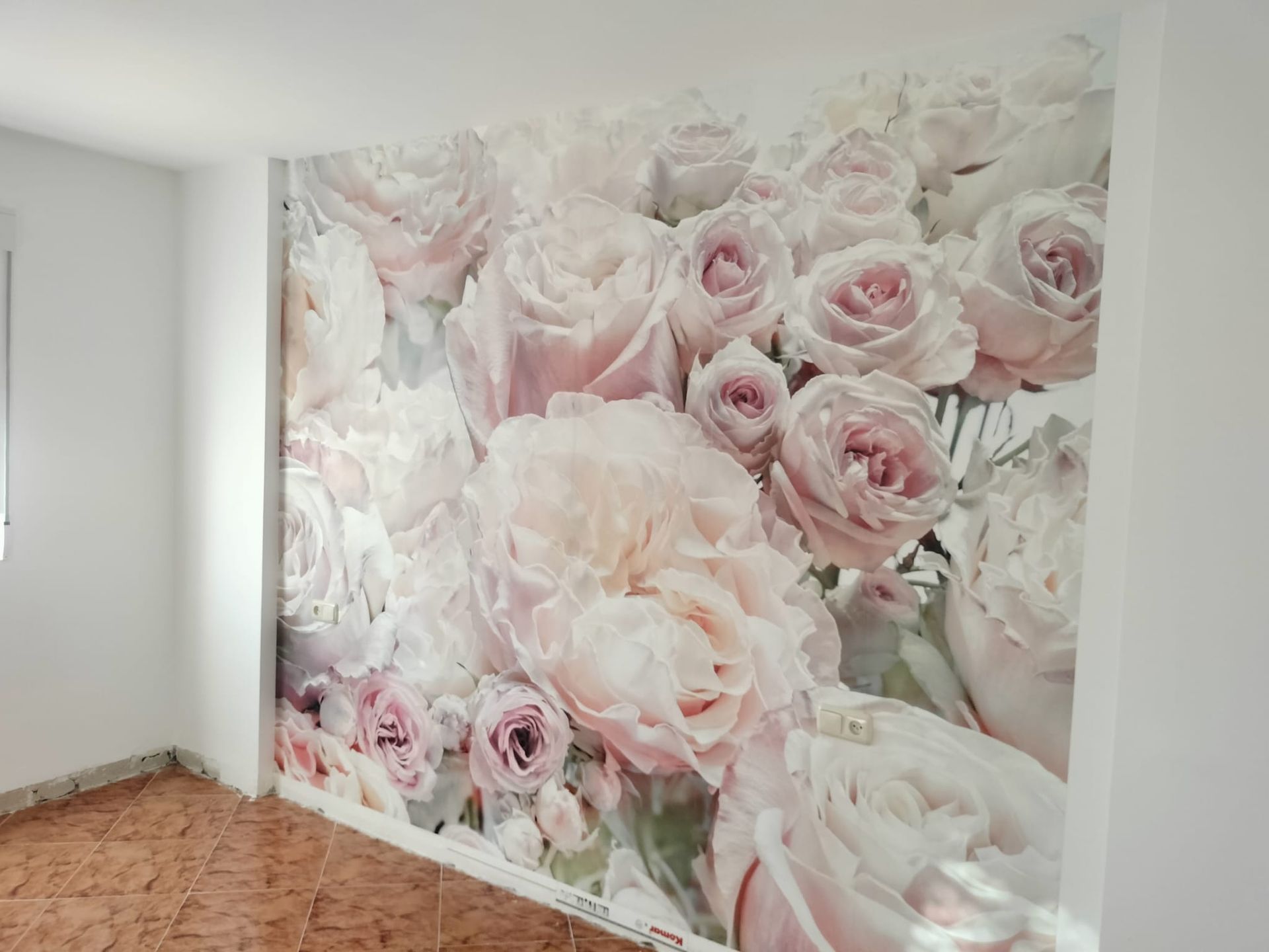 Gran mural de rosas rosadas en una pared blanca de una habitación luminosa con suelo de madera.