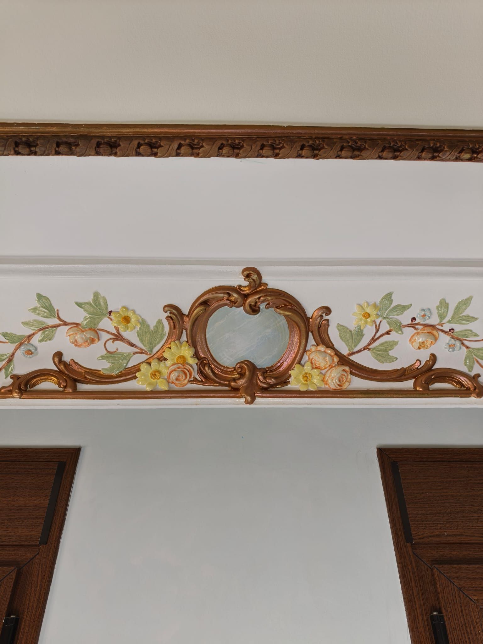 Mural decorativo floral con espejo ornamentado enmarcado en oro, sobre dos ventanas y una puerta.