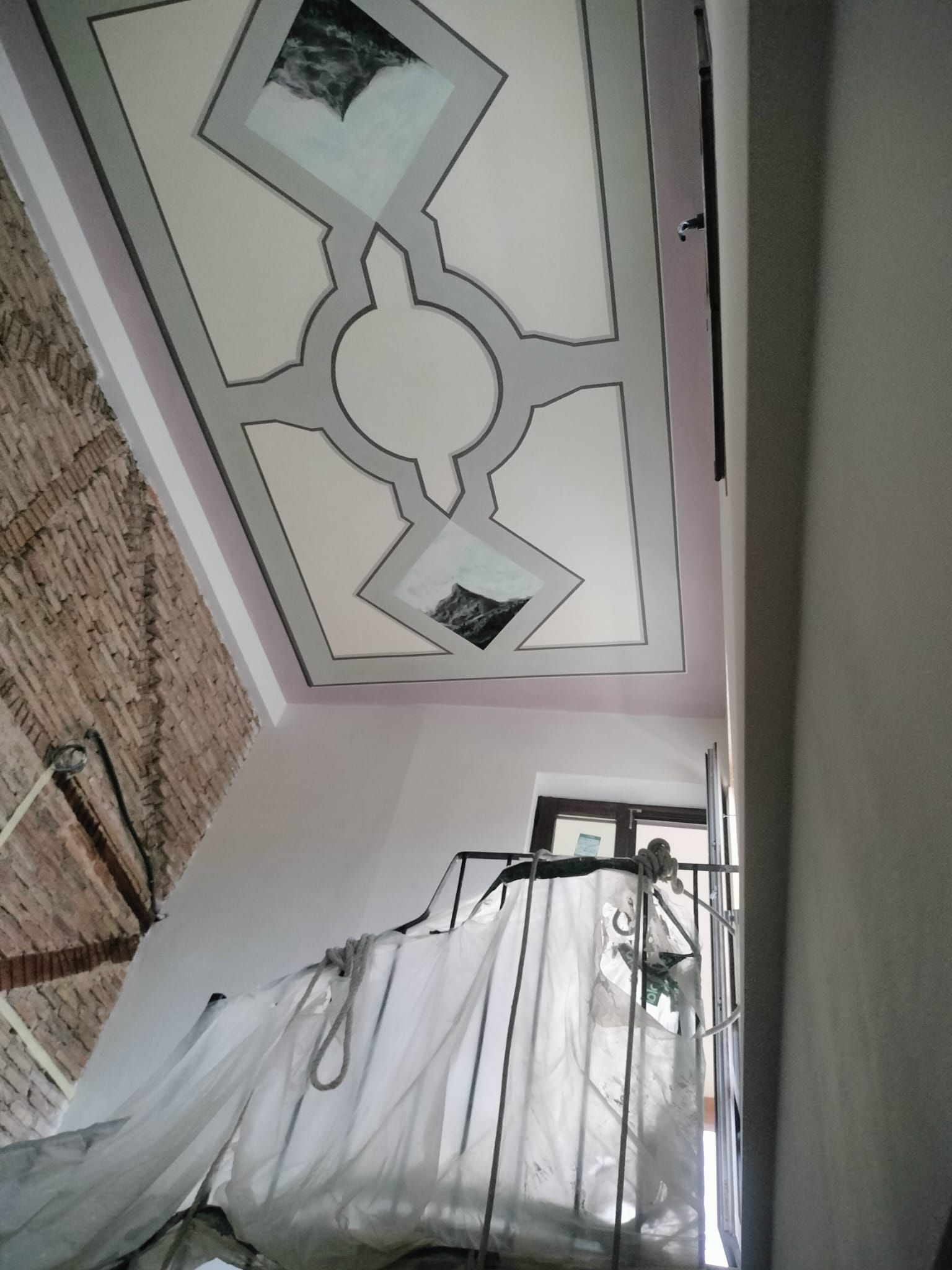 Techo interior con panel decorativo y pared rosa junto a una ventana con cortinas y cables colgantes.