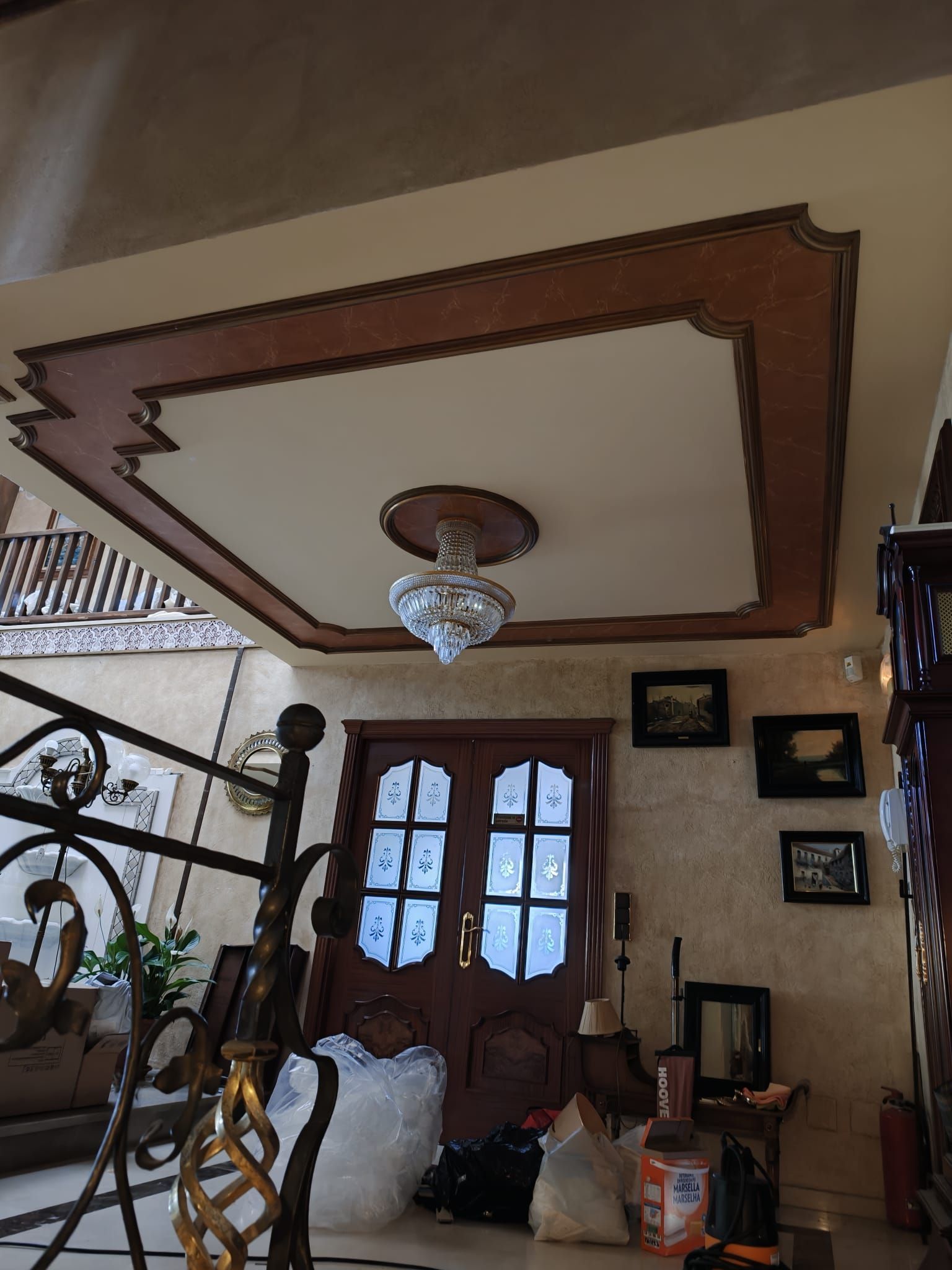 Vestíbulo ornamentado con puertas dobles de madera, lámpara de araña, escalera y cuadros enmarcados.