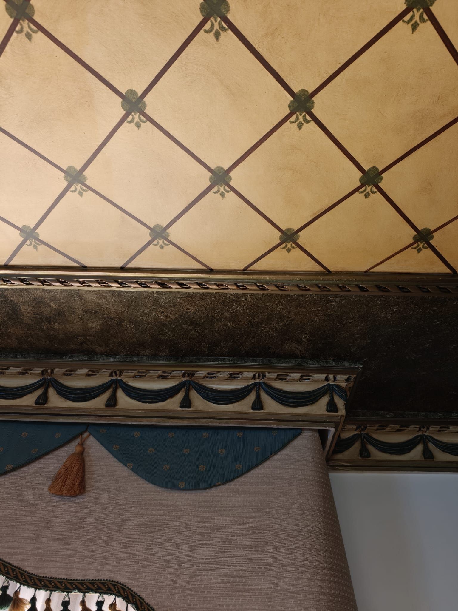 Techo decorativo con estampado de rombos beige, borde oscuro ornamentado y cenefa de cortina azul drapeada.