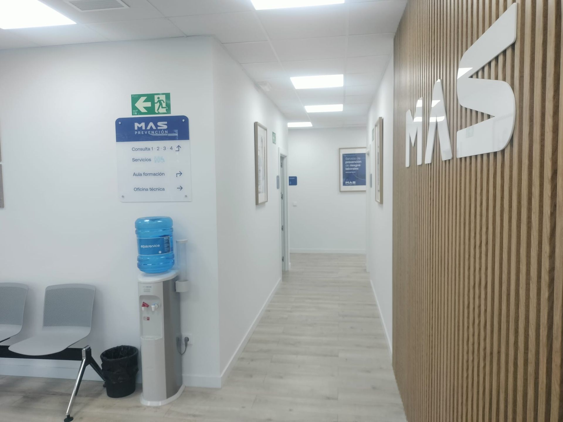 Pasillo de oficina moderno con paredes blancas, revestimiento de madera, sillas, dispensador