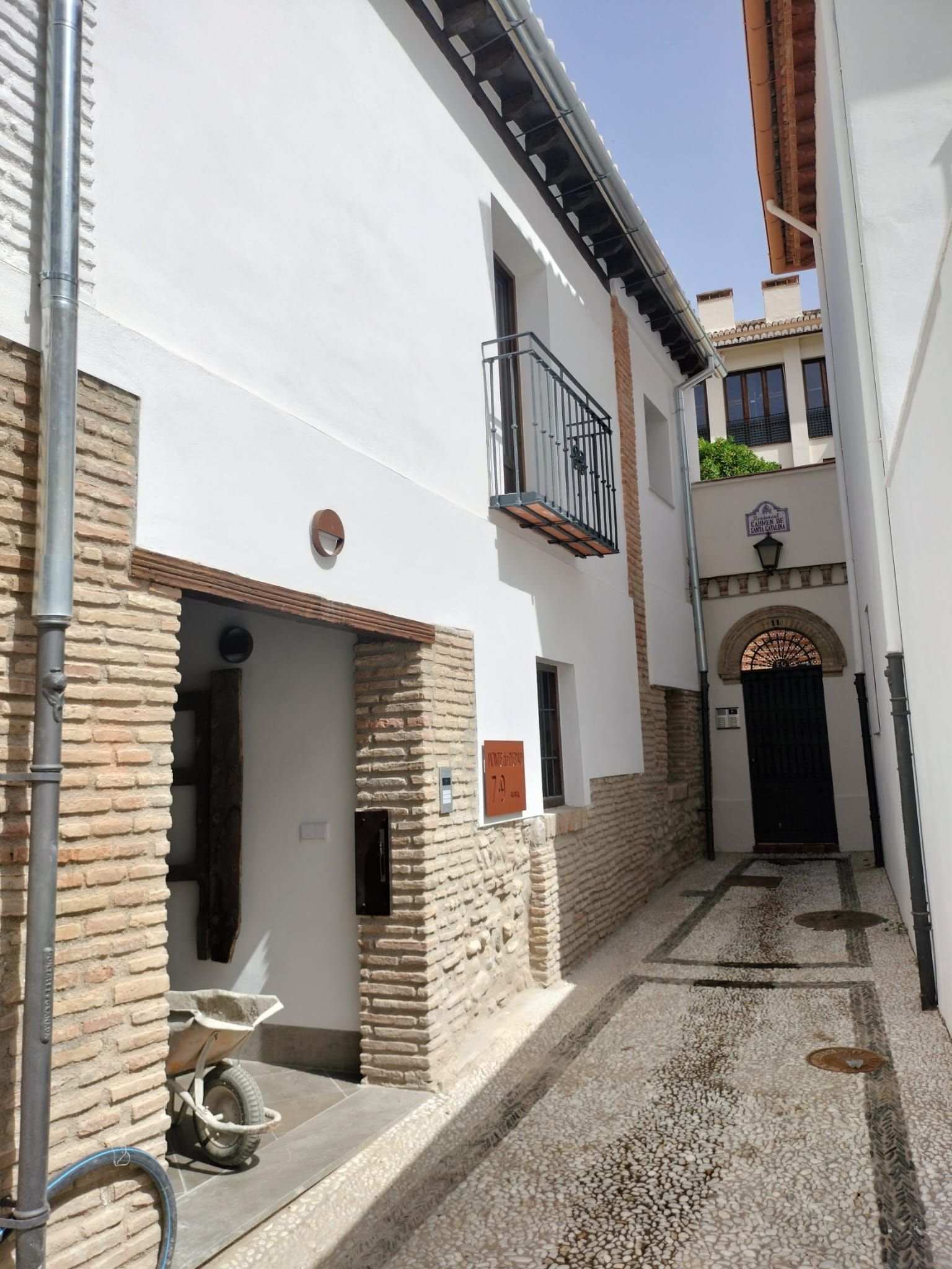Un estrecho callejón encalado con detalles de piedra, pequeños balcones y una puerta arqueada bañada por la luz del sol.