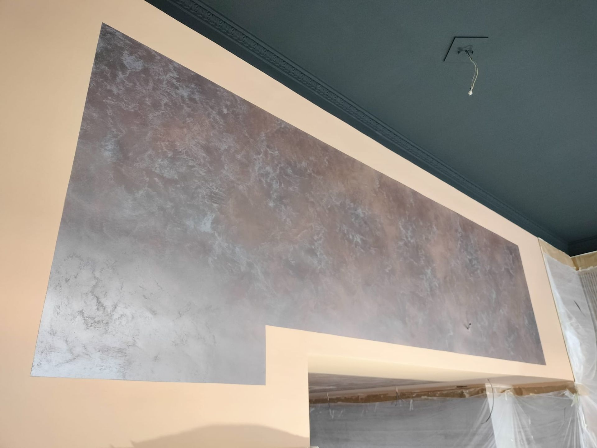 Pared con acabado texturizado gris sobre una puerta en una habitación con techo verde azulado oscuro.