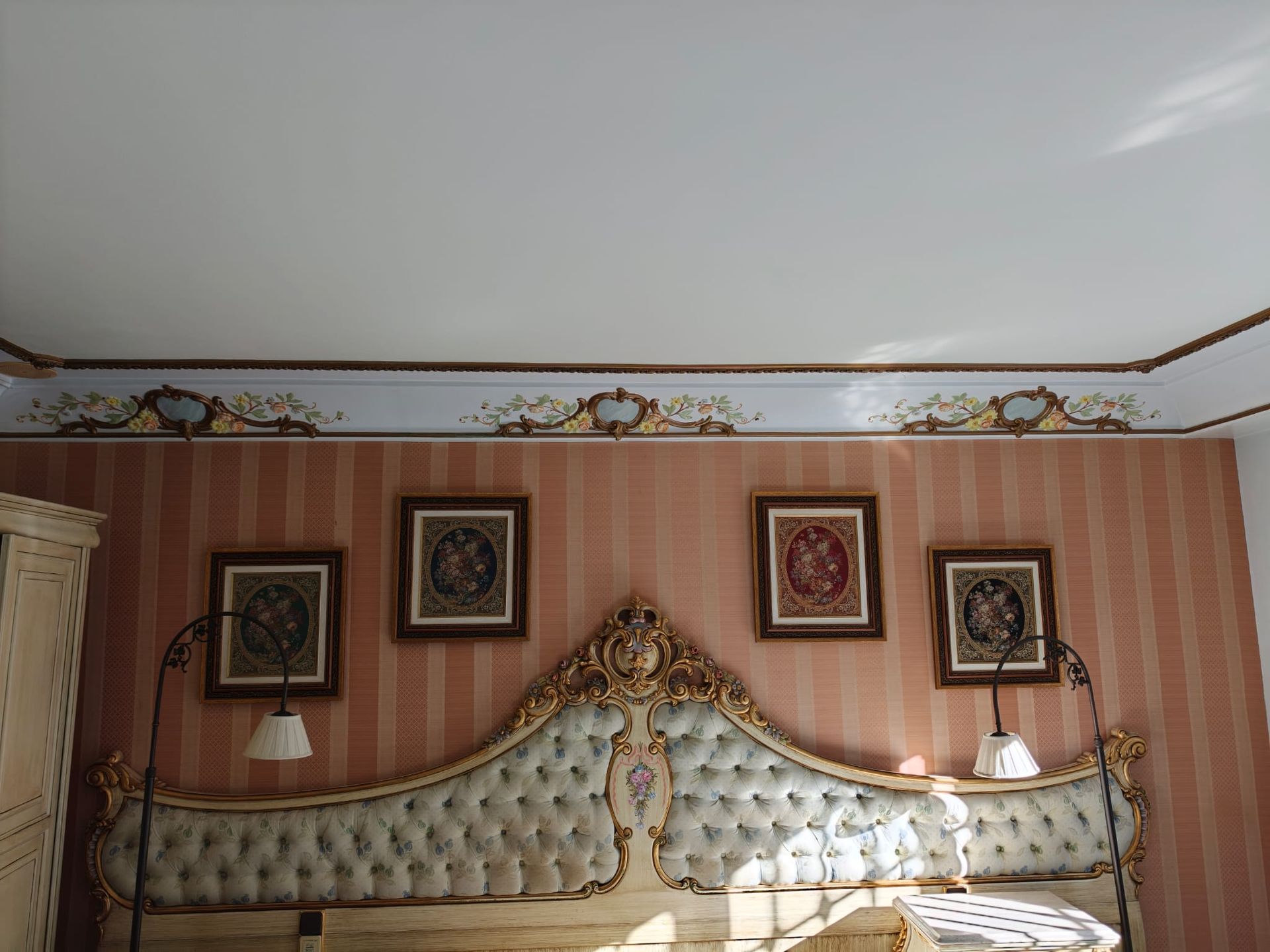 Elegante dormitorio con cabecero capitoné, cuadros enmarcados y papel pintado a rayas cálidas.