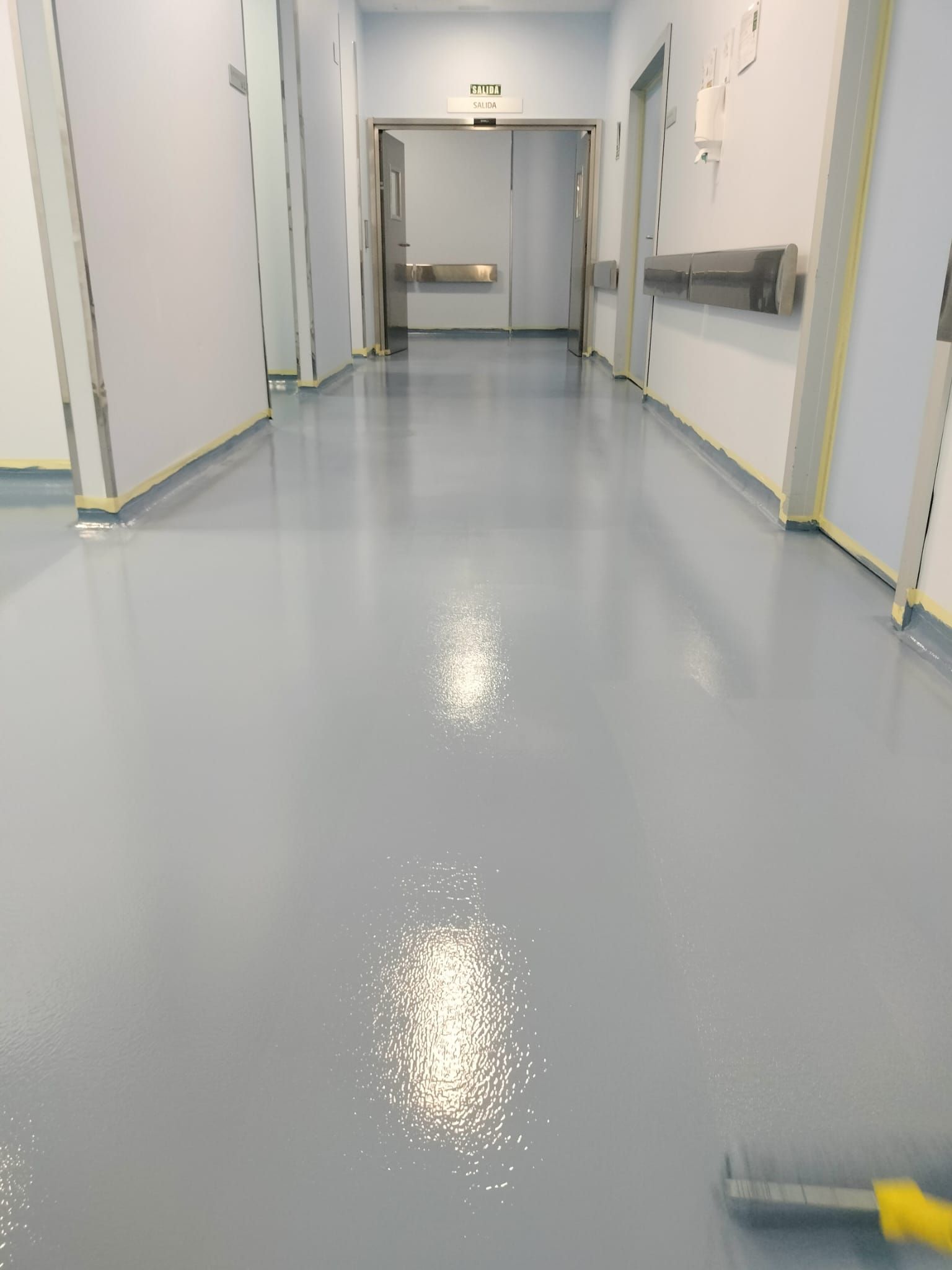 Pasillo vacío de hospital con suelo azul claro brillante y paredes blancas.