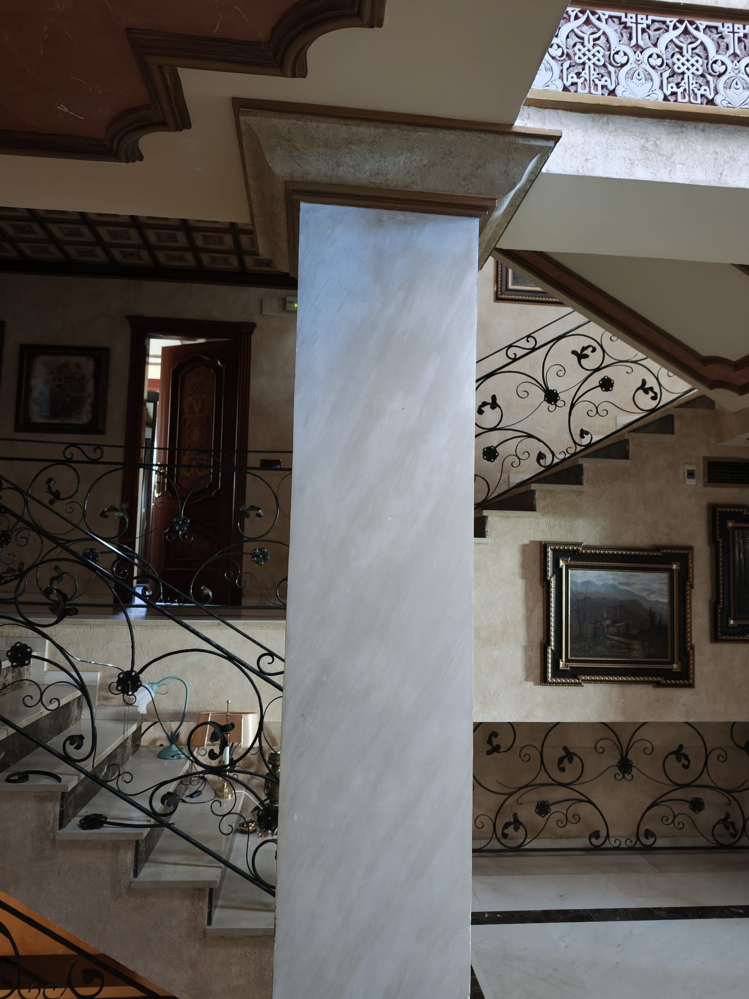 Escalera con barandillas negras ornamentadas y un pilar central de piedra en el interior de una vivienda.