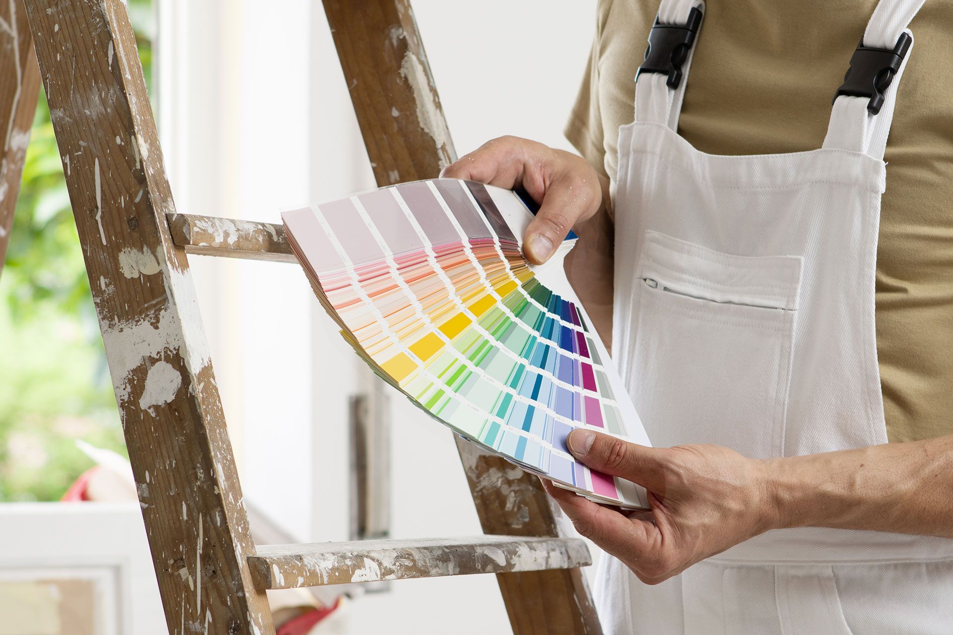 Eine Person hält eine Farbpalette vor einer Leiter.