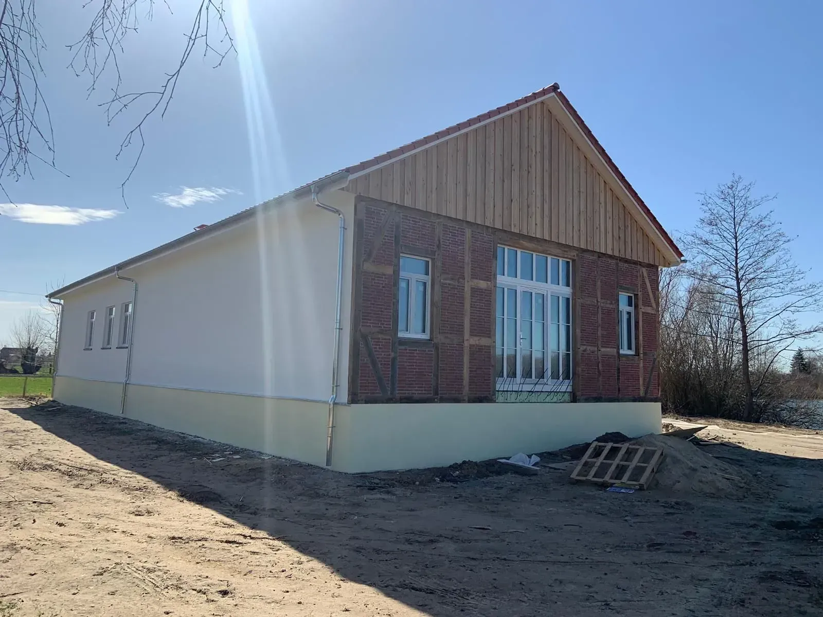 Neues Backsteinhaus im Bau mit weißer Fassadenverkleidung, gelegen auf einem sonnigen unbefestigten Grundstück.