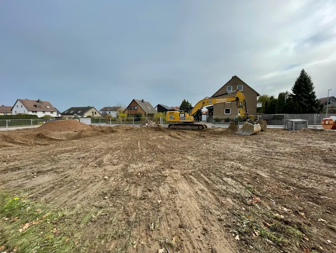 Baustelle mit Baggern, die unter bewölktem Himmel ein matschiges Grundstück in der Nähe von Häusern räumen