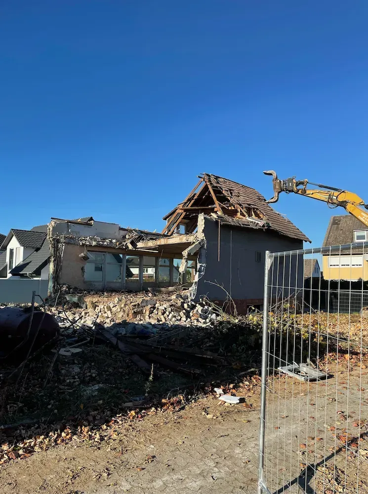 Abgerissenes Haus, Bagger räumt Schutt unter klarem, blauem Himmel