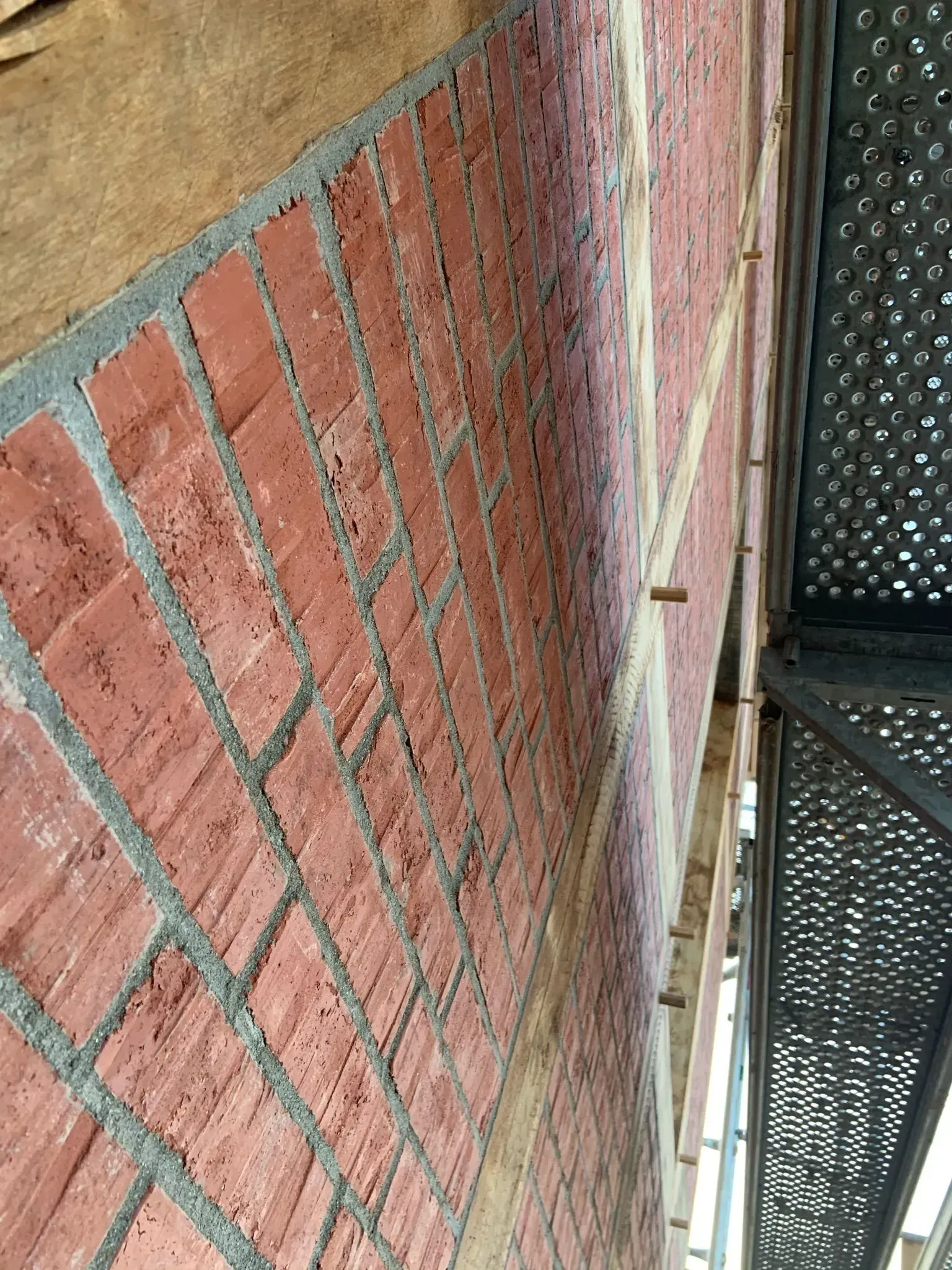 Rote Backsteinmauer neben einem Metallgittersteg und beigefarbener Stuckfassade