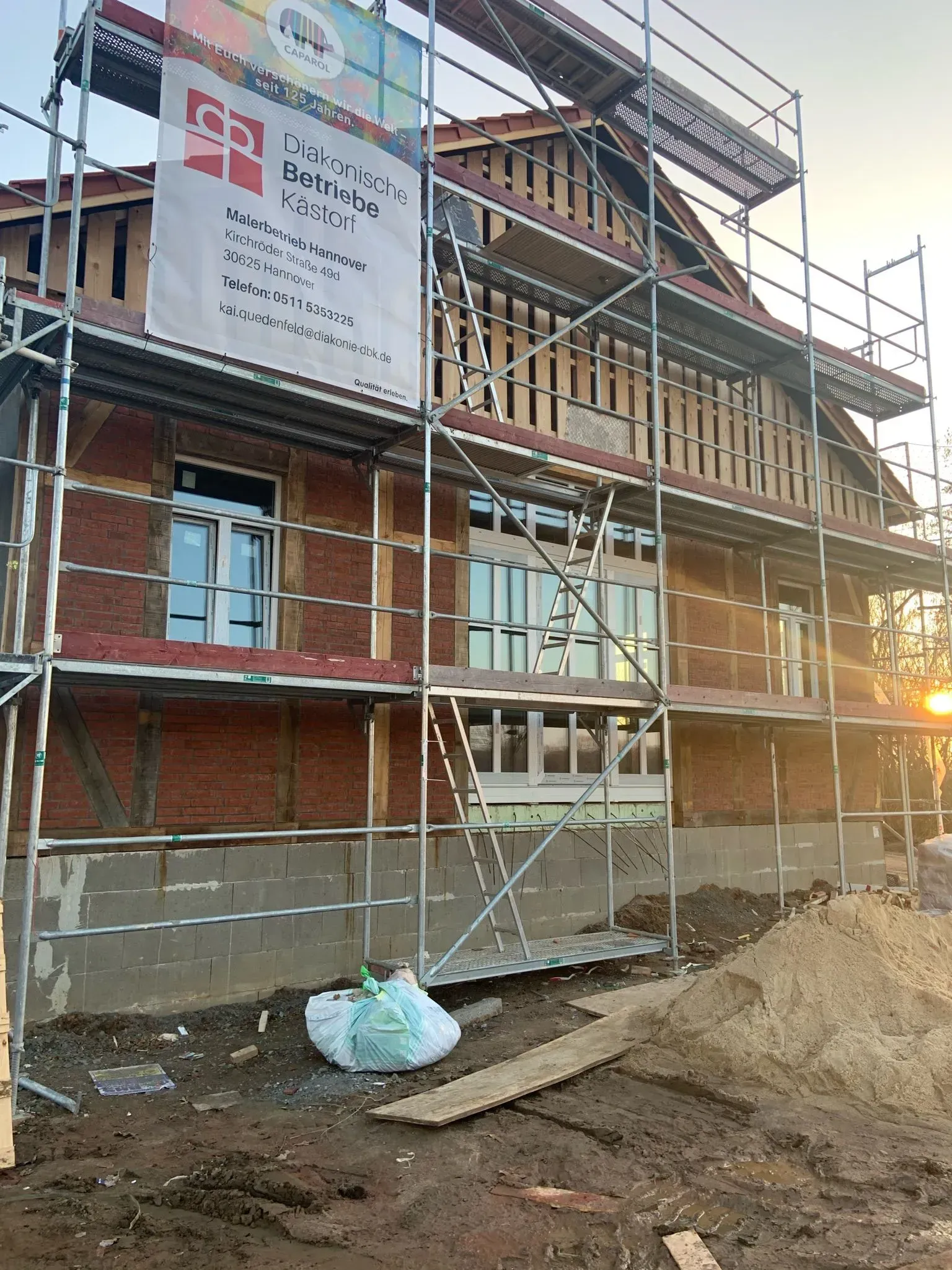 Backsteingebäude im Bau mit Gerüst, freiliegendem Fachwerk und dem Schein der untergehenden Sonne auf der rechten Seite.