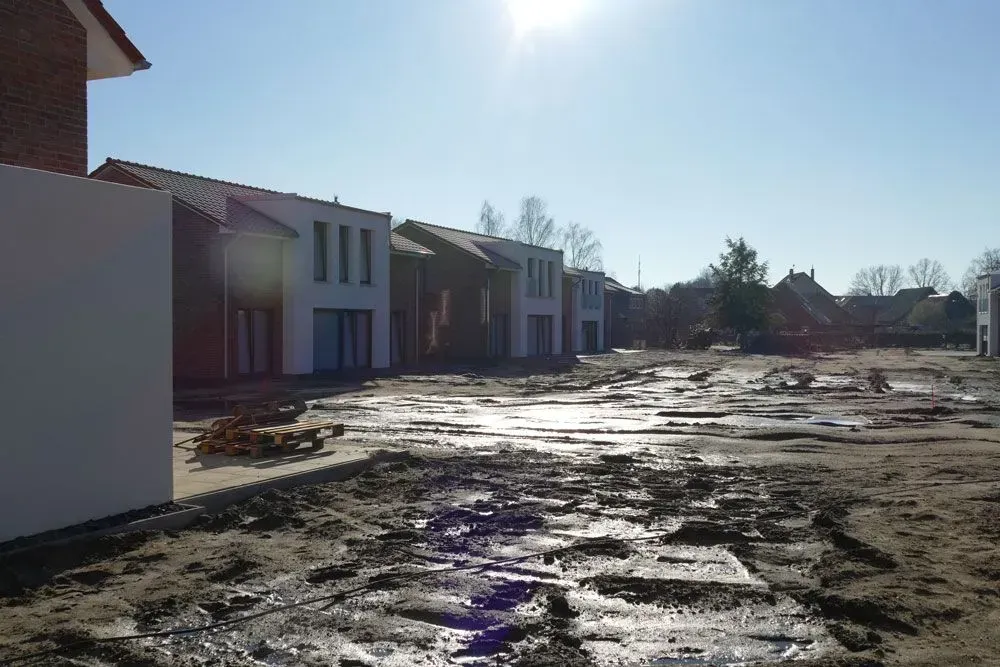 Eine Reihe moderner Häuser neben einer schlammigen, vereisten Baustelle unter strahlend blauem Himmel