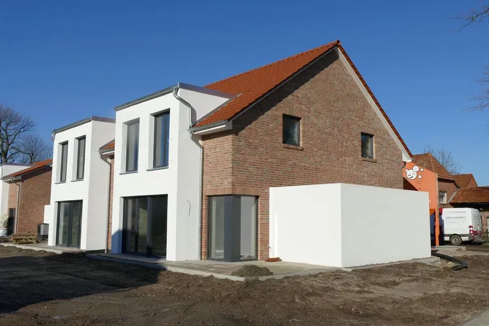 Modernes zweistöckiges Haus mit weißer und gemauerter Fassade und rotem Dach im Bau