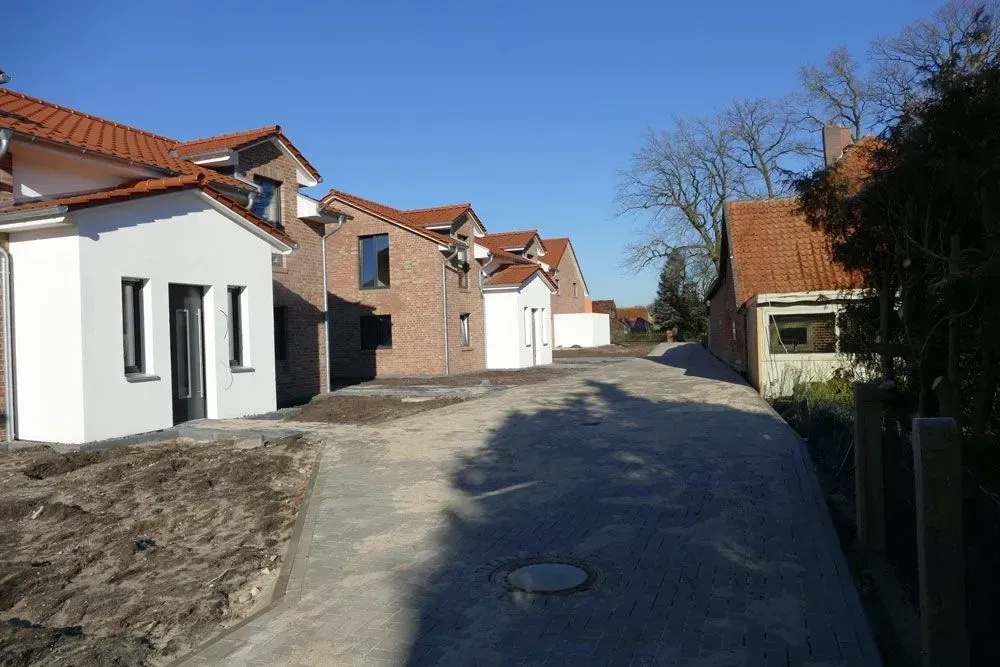 Ruhige Wohnstraße mit Häusern, blauem Himmel und einer schmalen, im Bau befindlichen Straße