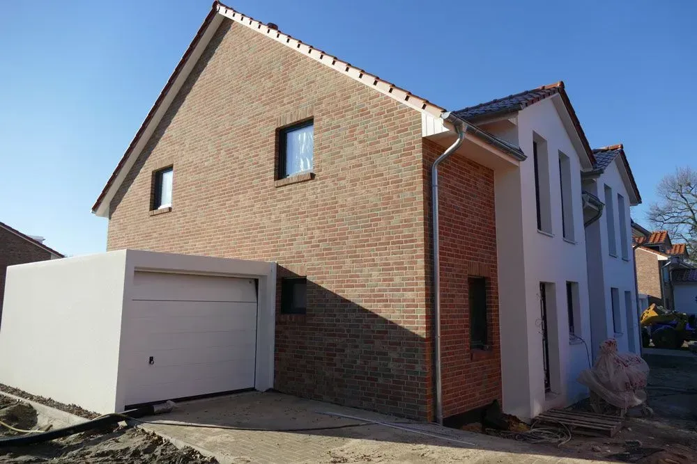 Backsteinhausfassade mit weißer Garage und schrägem Dach an einem sonnigen Tag
