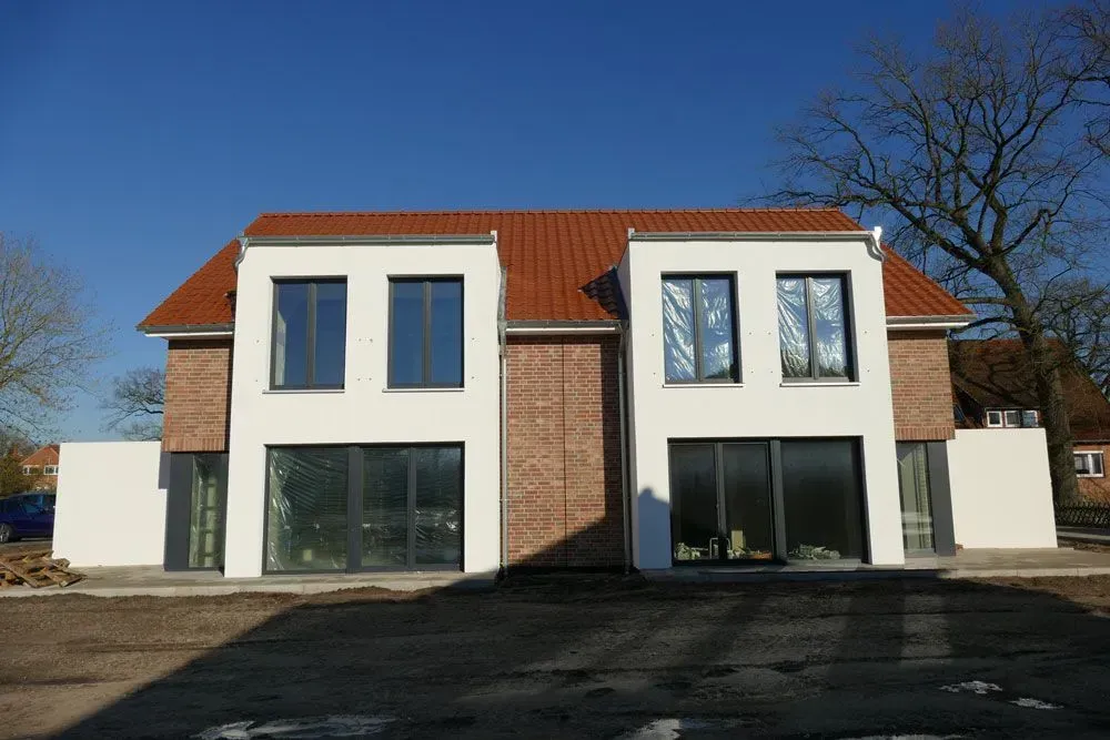 Modernes zweistöckiges Haus mit weißen Wänden, rotem Dach und großen Fenstern unter einem klaren blauen Himmel