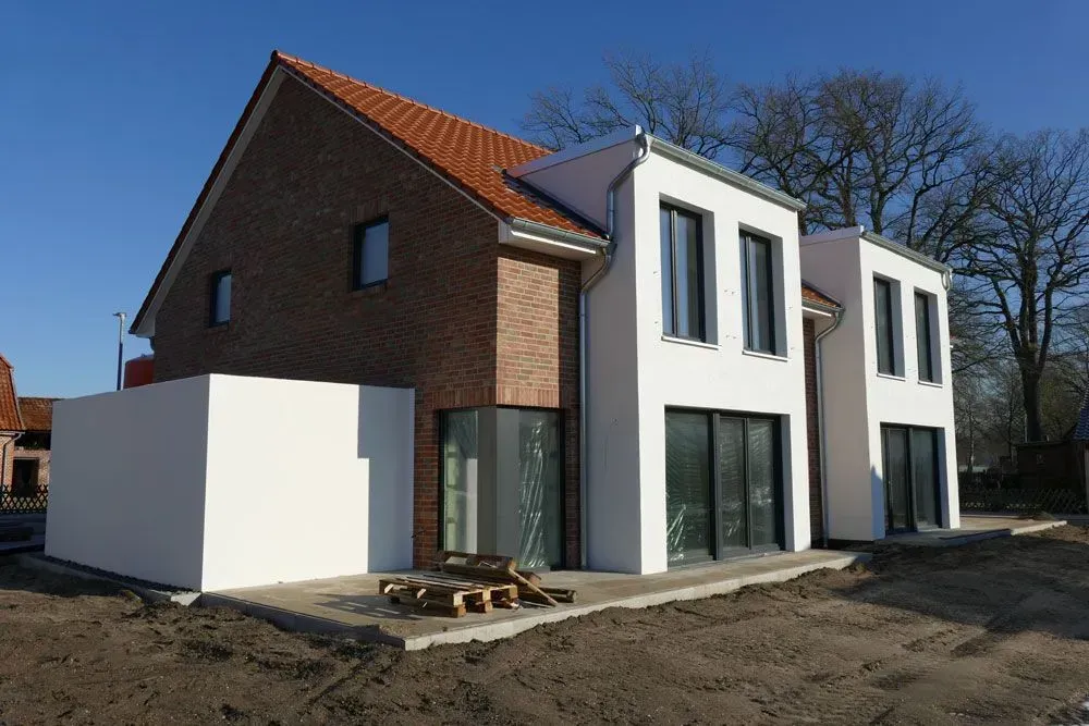 Modernes zweistöckiges Haus mit weißer Backsteinfassade, großen Fenstern und einem kleinen Garten unter klarem, blauem Himmel