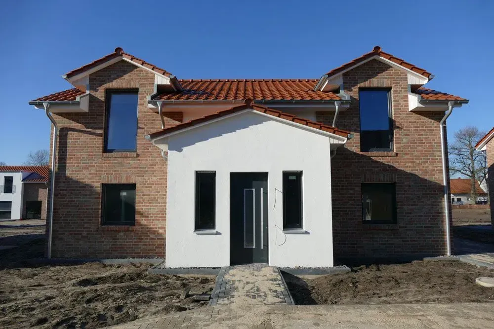Vorderansicht eines neuen zweistöckigen Hauses mit rotem Ziegeldach, Backsteinwänden und weißem Mitteleingang.