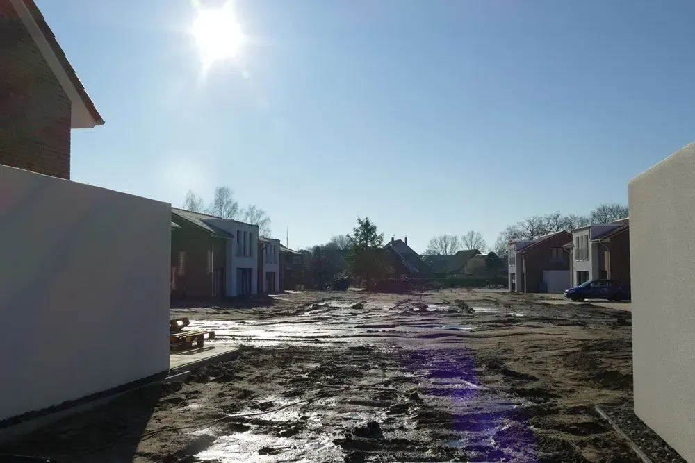 Eine sonnenbeschienene, schlammige Baustelle zwischen unfertigen Häusern unter einem klaren blauen Himmel