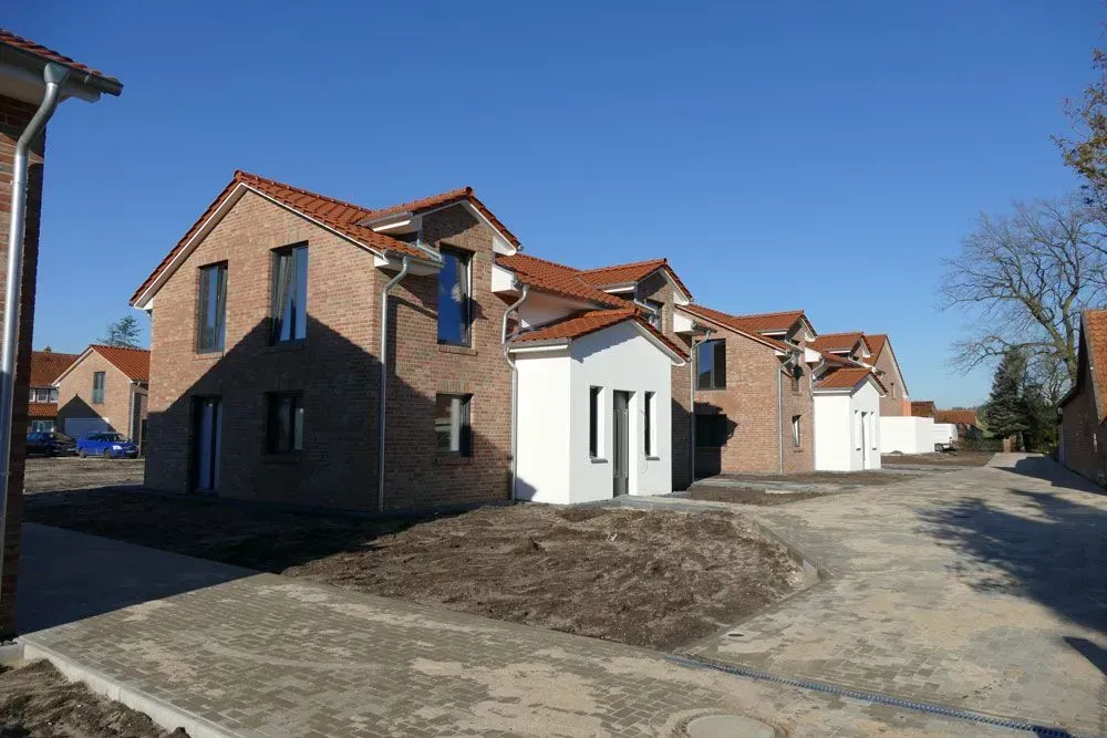 Eine Reihe neu gebauter Backsteinhäuser mit roten Dächern an einem Feldweg unter klarem, blauem Himmel