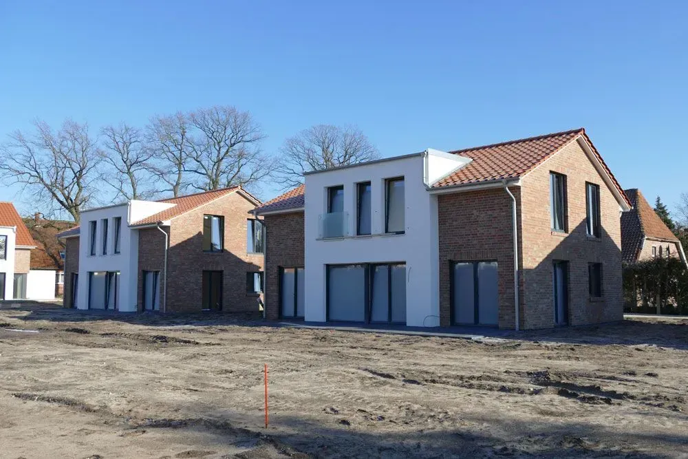 Neu gebaute, moderne Häuser mit Backstein- und weißen Fassaden auf einem unbebauten Grundstück unter klarem, blauem Himmel