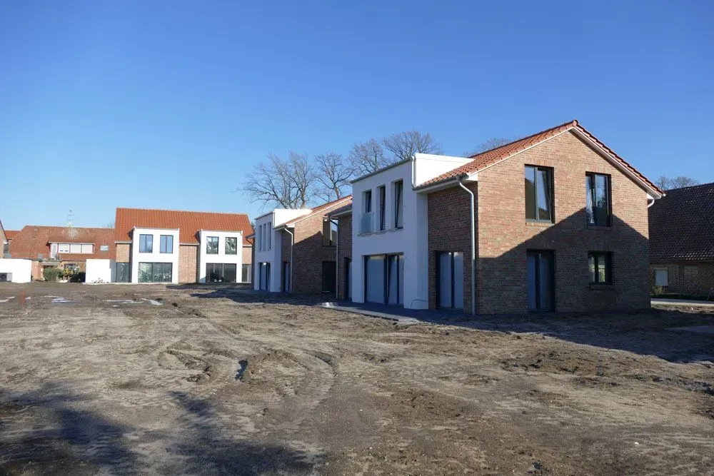 Neue Backsteinhäuser werden an einem sonnigen Tag auf einem unbebauten Grundstück gebaut.
