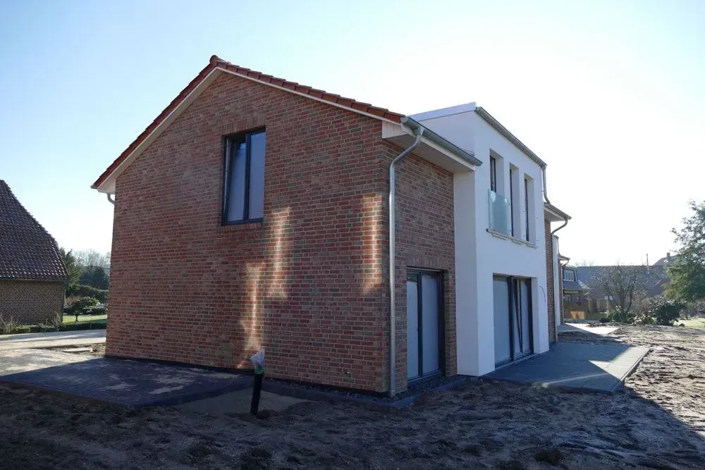 Hausfassade aus Backstein mit weißen Zierelementen und dunklem Dach an einem sonnigen Tag