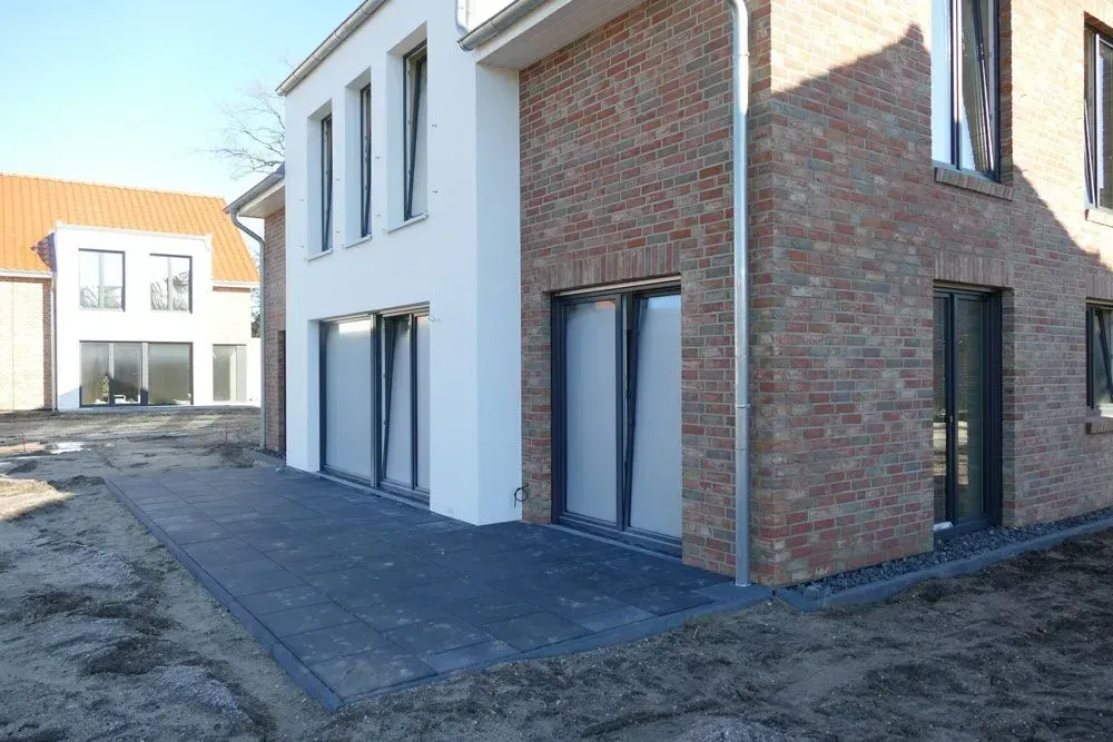 Modernes Backsteinhaus mit weißen Zierelementen und gepflasterter Terrasse in einem neuen Wohngebiet
