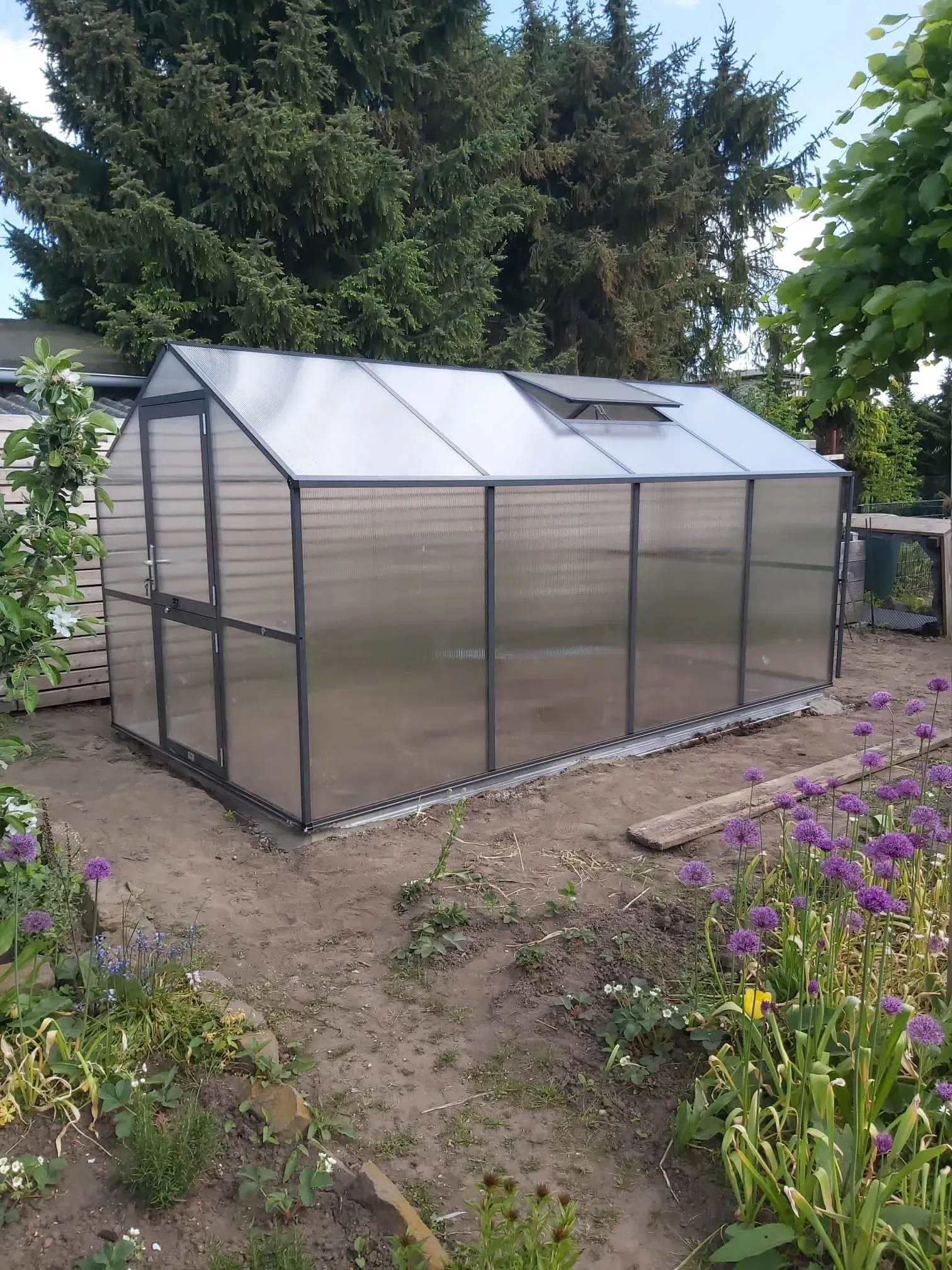 Referenzbild: Kleines Gewächshaus im abgelegeneren Teil des Gartens, umgeben von Blumenbeeten