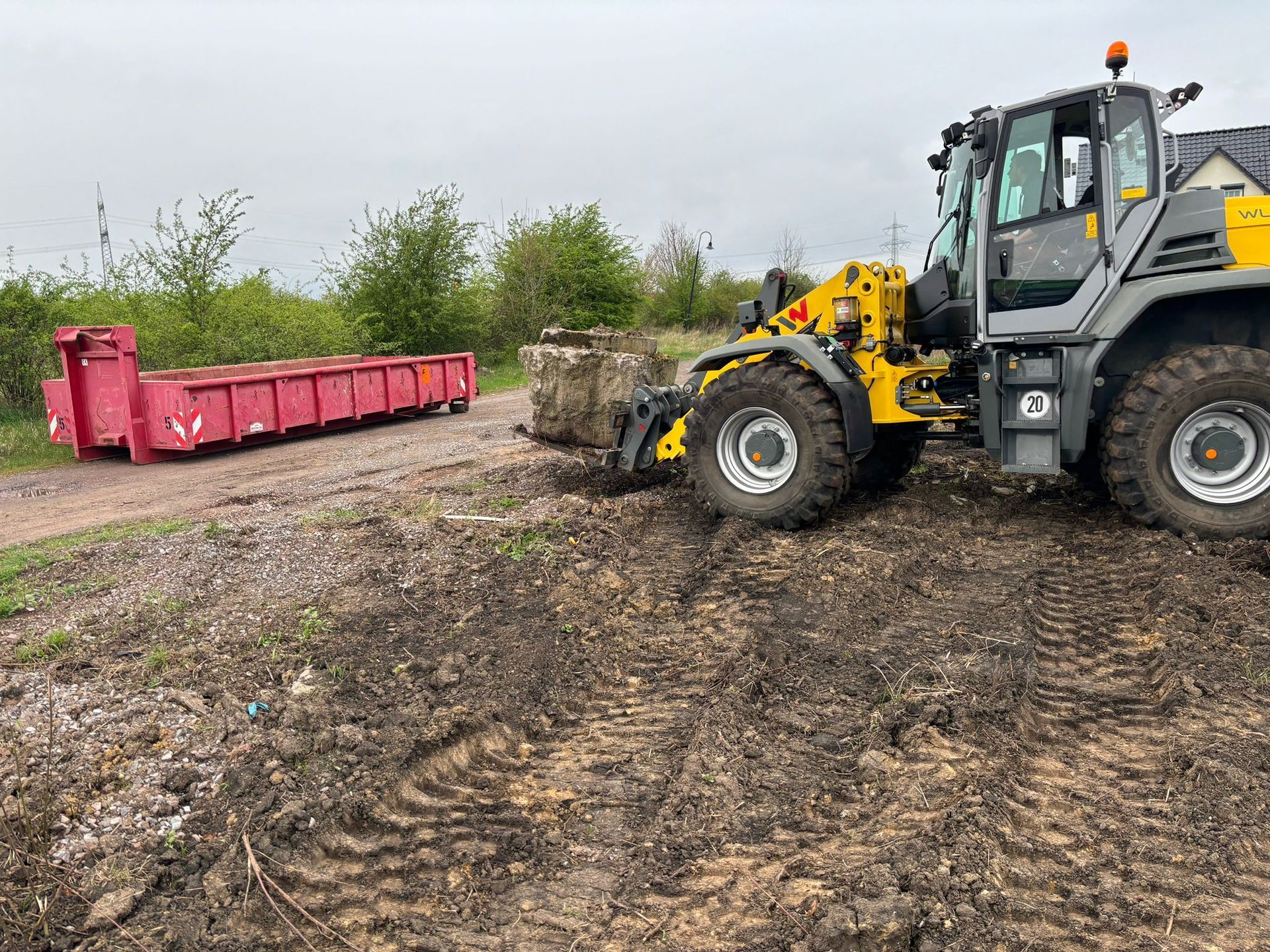 Referenzbild: Eine Planierraupe bewegt Erde auf einem Feld neben einem roten Müllcontainer.